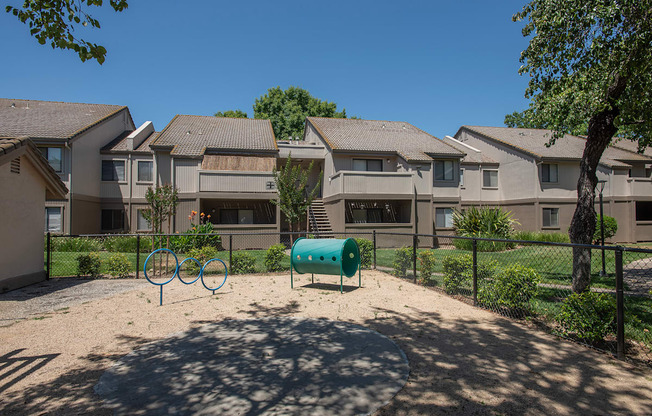 A dog park with a green barrel and two blue rings in front of apartment buildings at Zinfandel Village Apartments, California, 95670