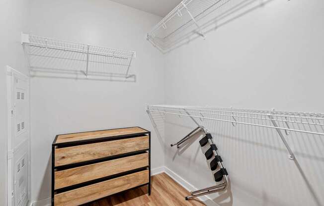A white closet with a wooden chest of drawers and a metal rack.