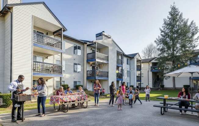 A group of people are gathered in a courtyard with a man grilling food on a barbecue.