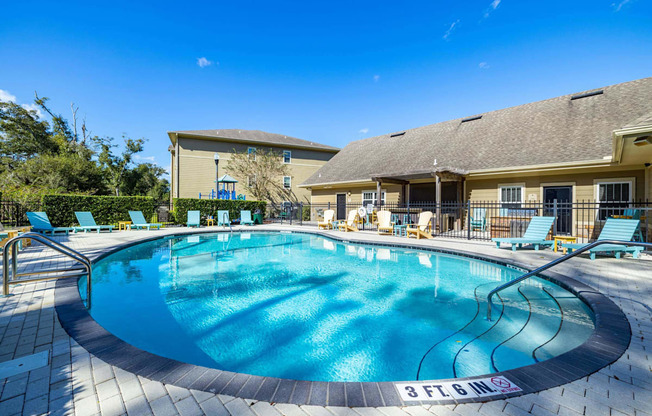 A large outdoor swimming pool with lounge chairs and a building in the background.