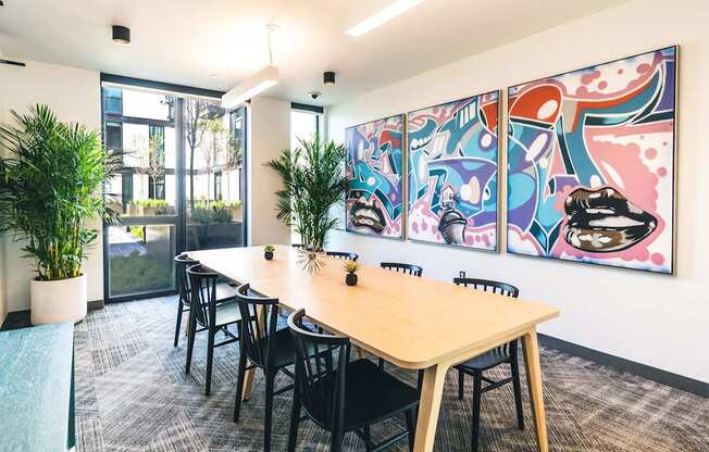 A conference room with a long table and chairs, a potted plant, and a colorful mural on the wall.