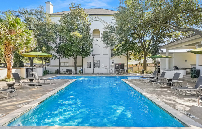 A large swimming pool surrounded by lounge chairs and trees.