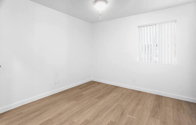 an empty room with white walls and wooden floors and a window