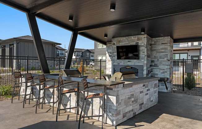 A stone barbecue with a grill on top is surrounded by chairs.