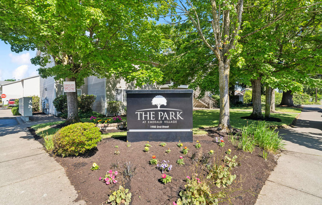 a park with a sign and trees and flowers