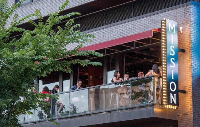 A group of people are sitting on a balcony of a building with a sign that says