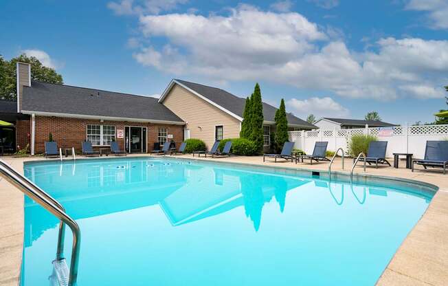 A large swimming pool in front of a building with a blue sky and clouds in the background.