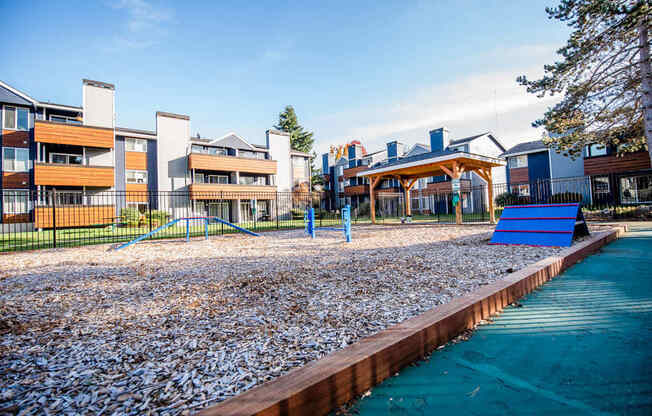 A playground with a blue slide and a pebble-covered area. at Northpoint Apartments, Washington, 98407