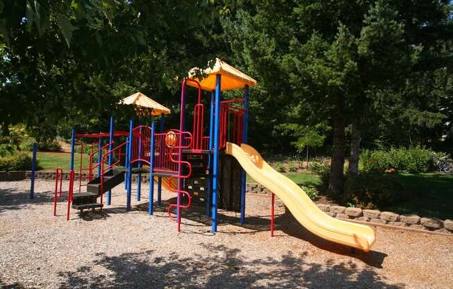 A playground with a yellow slide and red and blue structures at Wilsonville Summit Apartments, Wilsonville  97070