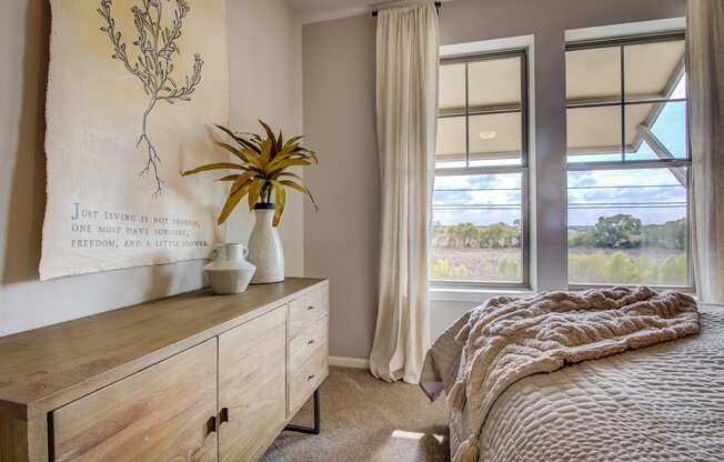 a bedroom with a large window and a dresser with a plant on it