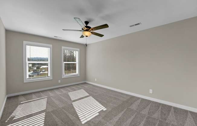 an empty living room with a ceiling fan and two windows