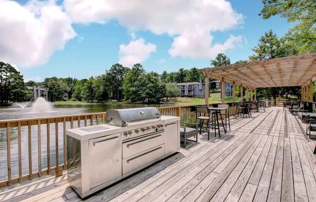 a grill on a deck next to a lake with tables and chairs