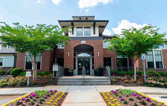 the front entrance of a brick building with trees and flowers