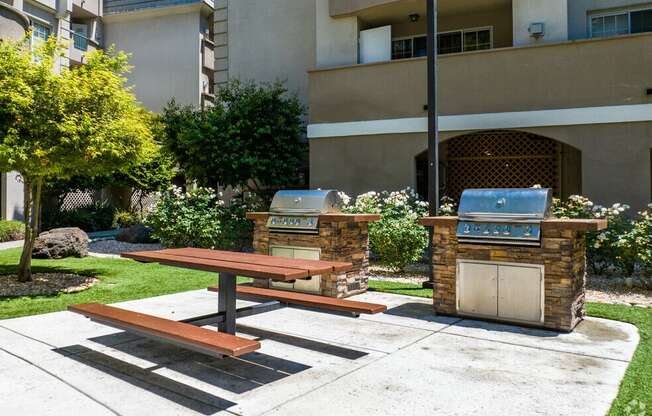a picnic table and two barbecue grills in front of an apartment building