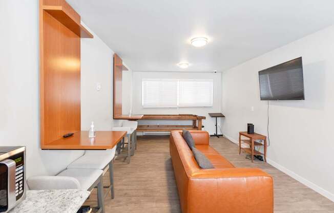 A modern resident lounge with a long orange sofa and a television on the wall at our Billings apartments in MT.