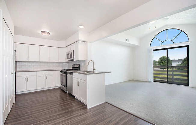 A kitchen with white cabinets and a living room with cathedral ceiling at The Crossings Apartments, Grand Rapids, MI, 49508