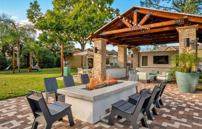 Propane fire pit with black lounge chairs and the shaded outdoor lounge in the background