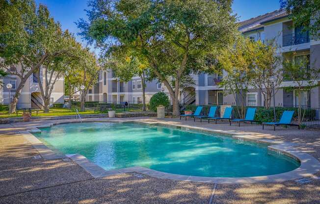 A close-up view of the swimming pool at Saxony at Chase Oaks Apartments in Dallas, TX, with lounge chairs and trees in the background, showcasing a relaxing outdoor space.