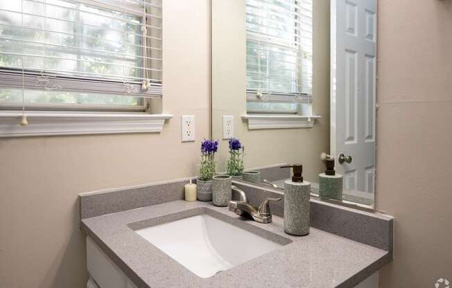 A bathroom with a sink, mirror, and a window with blinds.