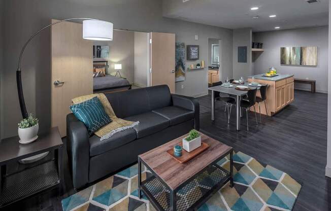A black couch with a blue pillow and a small potted plant on a table.