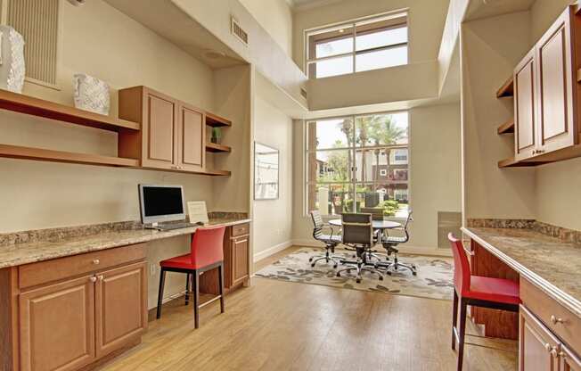 a room with a computer desk and chairs and a large window