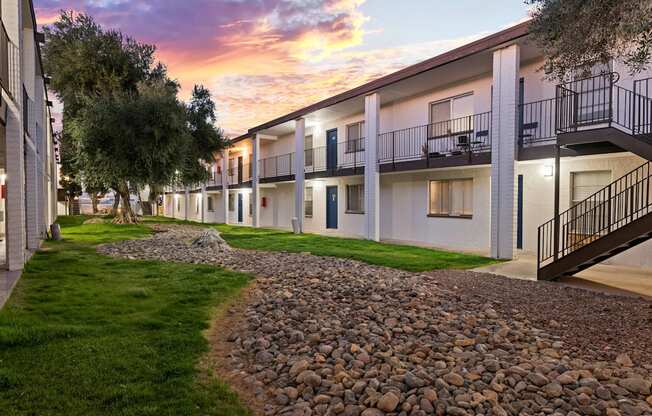A sunset view of apartment buildings with balconies and a gravel path.