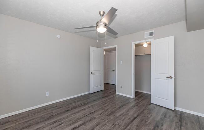 A spacious room featuring light gray walls, laminate flooring, and a ceiling fan. Two white doors lead to closets, and there is a small white light fixture on the ceiling. Natural light may enter through the doors, creating a bright and airy atmosphere.