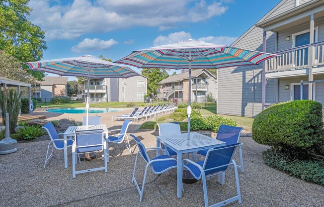 Poolside seating with a table and chairs under a striped umbrella at Laurel Parc apartments in Shreveport, LA.