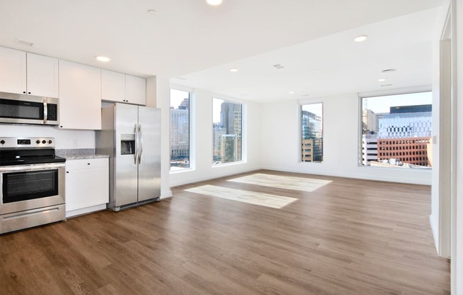 an empty living room with a kitchen and a large window
