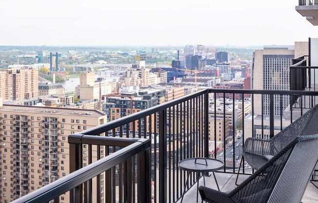 A balcony with a chair and table overlooking a cityscape.