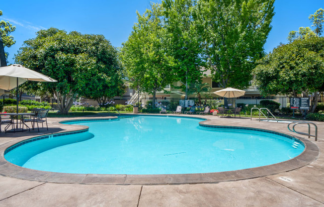 a swimming pool with trees and umbrellas next to a resort style pool