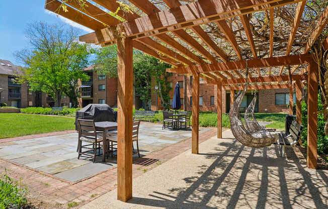 A wooden pergola provides shade over a patio with a table and chairs.