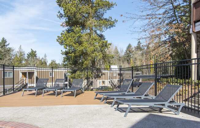 a patio with lounge chairs and a pool with trees in the background