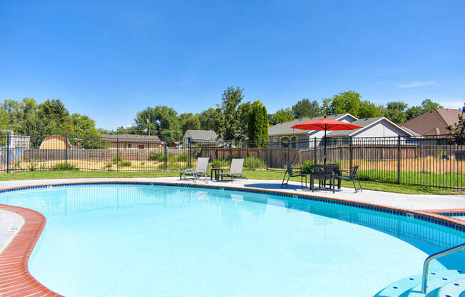 our resort style swimming pool is next to our yard with chairs and an umbrella