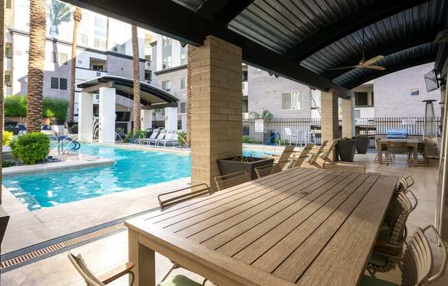 A wooden table is in the foreground of a patio with a pool.