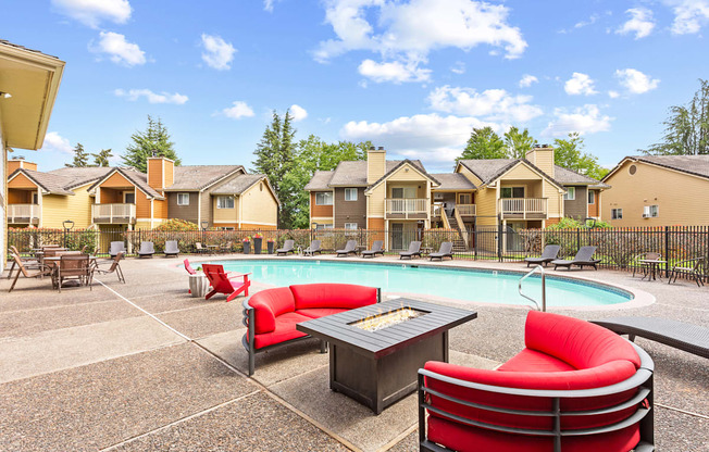 A pool area with red chairs and a hot tub in front of apartment buildings.