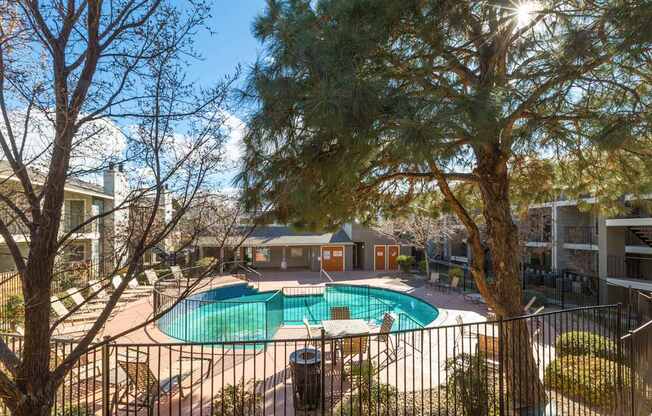 A pool surrounded by a fence with a tree in the foreground.