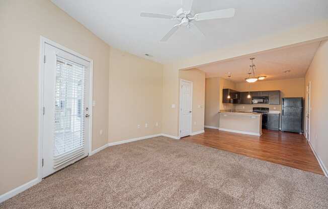 an empty living room with a ceiling fan and a kitchen