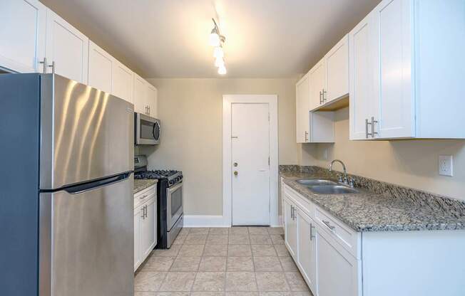 Lewis Manor Phase 3 renovated kitchen with white cabinetry, light marble counters, and stainless steel appliances.