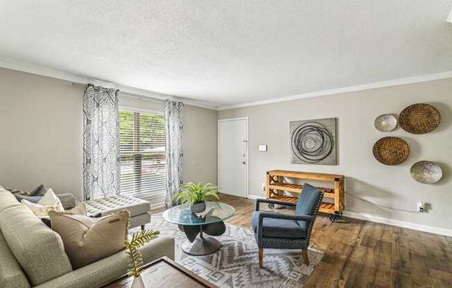 A living room with a grey couch, a blue chair, a glass coffee table, and a wooden shelf with baskets on it.