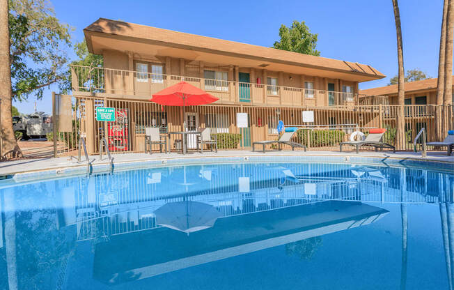 A swimming pool in front of a building with a red umbrella.