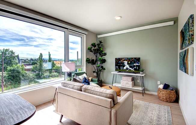 Apartments for Rent Seattle WA - Metroline Flats - Bright Spacious Living Room with Large Wall-to-Wall Window, Wood-Style Flooring, and Sage Green Accent Wall