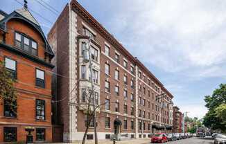 A row of red brick buildings line a tree-lined street.
