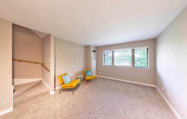 A room with a carpeted floor and two yellow chairs with blue cushions.