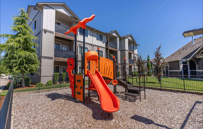 A playground with a slide and a climbing frame in front of a residential building at Timberridge Place Apartment Homes, Albany, OR