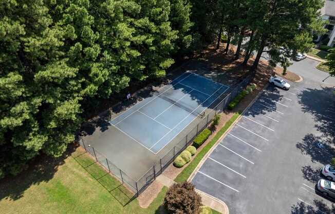 A tennis court is surrounded by a parking lot and trees.