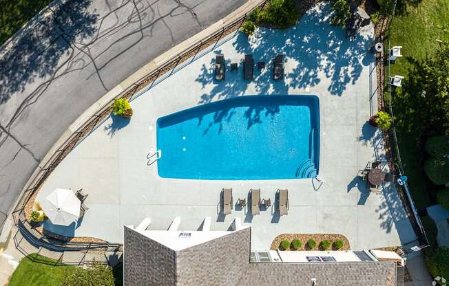 An aerial view of a swimming pool surrounded by a concrete patio and a building.