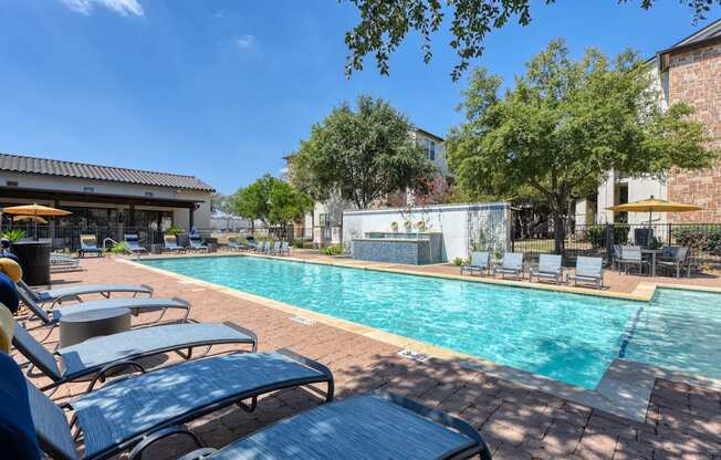 A pool surrounded by lounge chairs and trees.