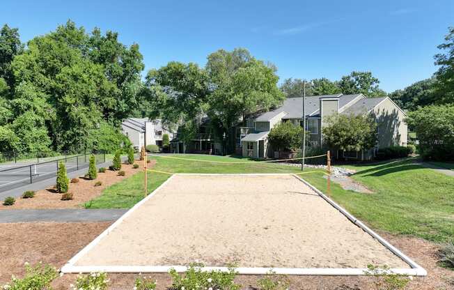 A sand volleyball court is surrounded by trees and houses.