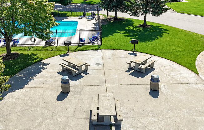 A concrete patio with four benches and a pool in the background.